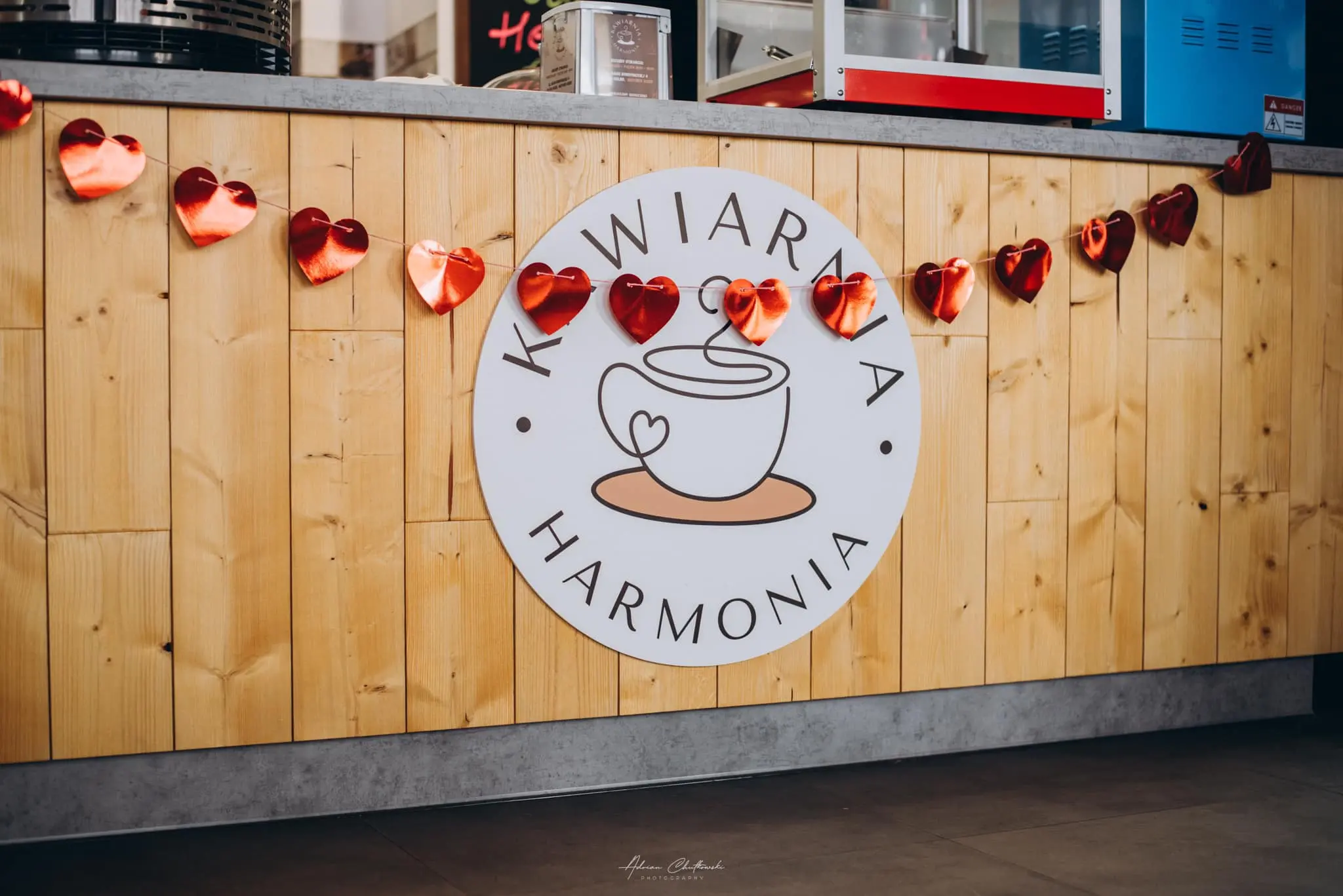 Drewniana ściana z okrągłym logo Kawiarni Harmonia i dekoracyjnymi sercami w Kolnie